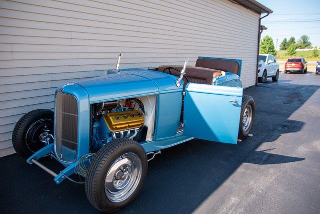 Blue hot rod with an exposed gold engine, parked next to a building, door open.