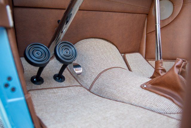 Close-up of a car's interior, showing brown pedals, tan carpet, and brown upholstered panels.