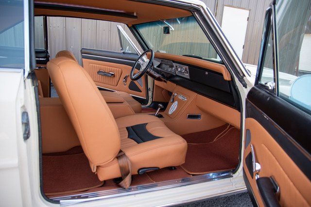 Tan and black interior of a classic car, with open doors, showing seats and dashboard.