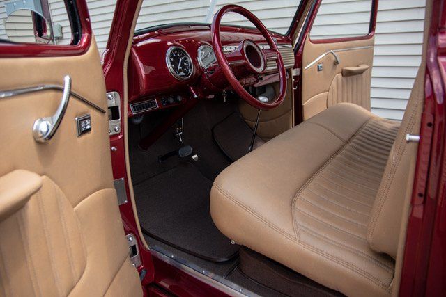 Interior of a classic red car with tan leather seats and dashboard; door open.