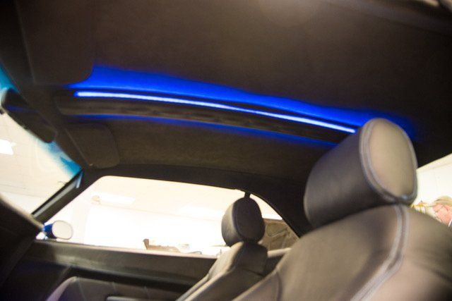Interior car view with blue overhead lighting, black seats, and a window view.