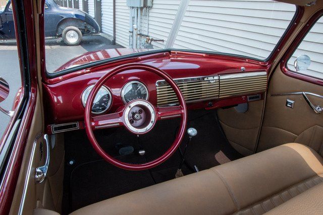 Interior view of a classic red car with a tan bench seat, dashboard, and steering wheel.