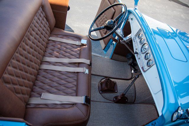 Interior view of a classic blue car with brown quilted seats, seatbelts, and steering wheel.