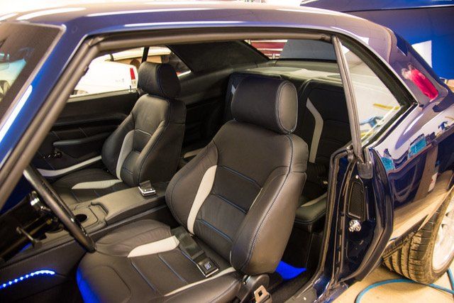 Interior of a blue classic car with black and gray seats, a center console, and blue under-seat lighting.