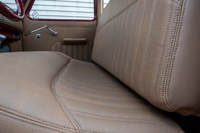 Tan leather bench seat in an old truck, with a detailed stitched pattern and armrest visible in the interior.