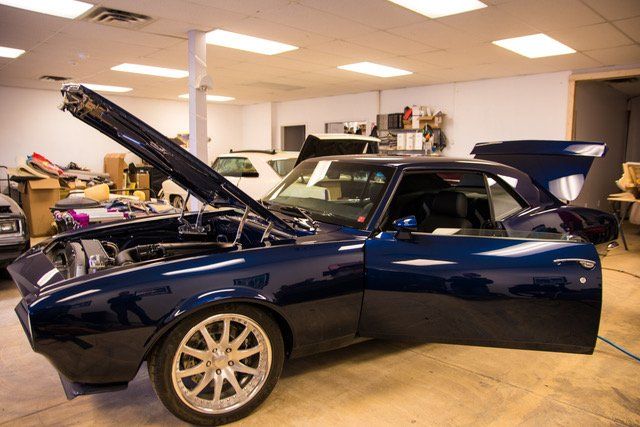 Dark blue classic car with open hood and door in a workshop.