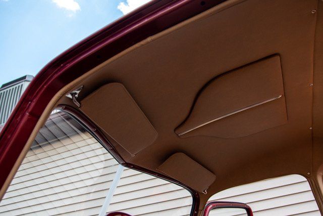 Interior view of a classic car's roof with tan headliner and sun visors against a blue sky.
