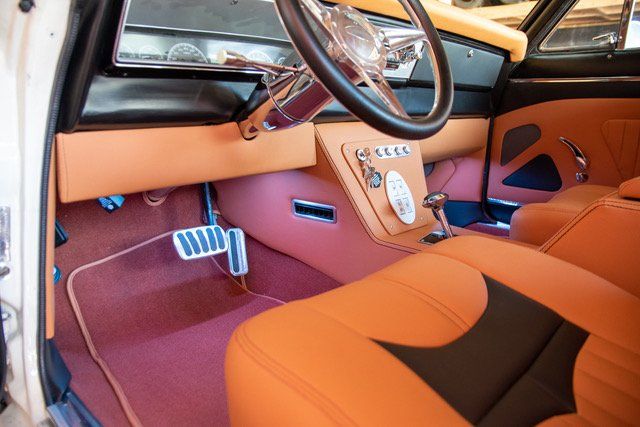 Custom car interior, orange and black leather, steering wheel, center console, red carpet.