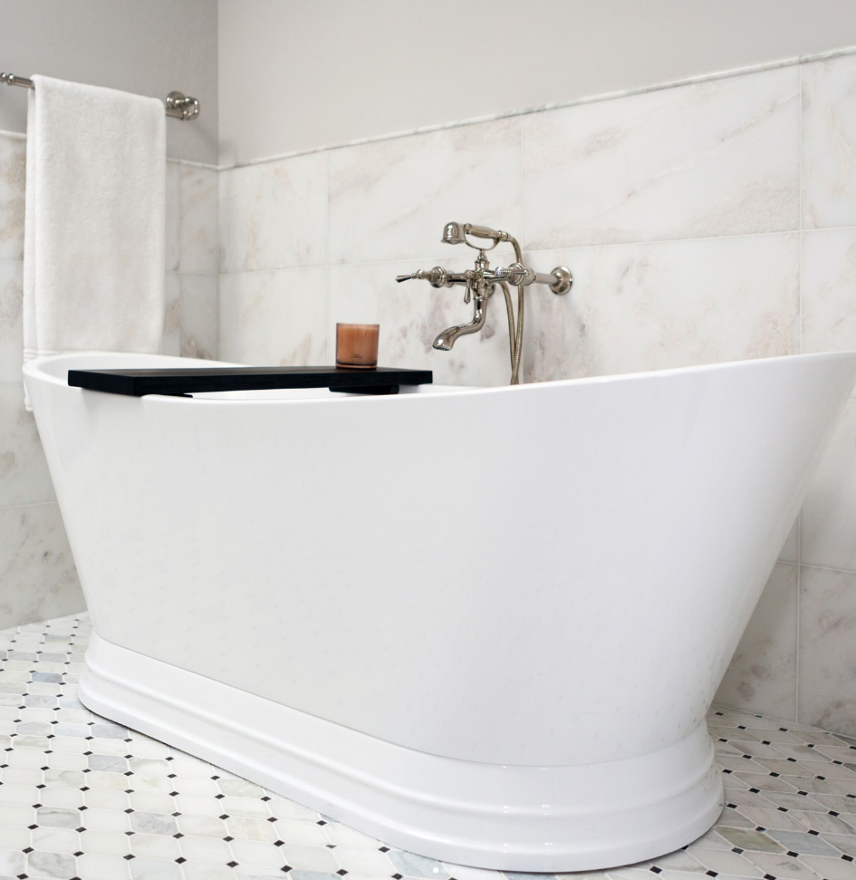 A white bathtub in a bathroom with a candle on a tray
