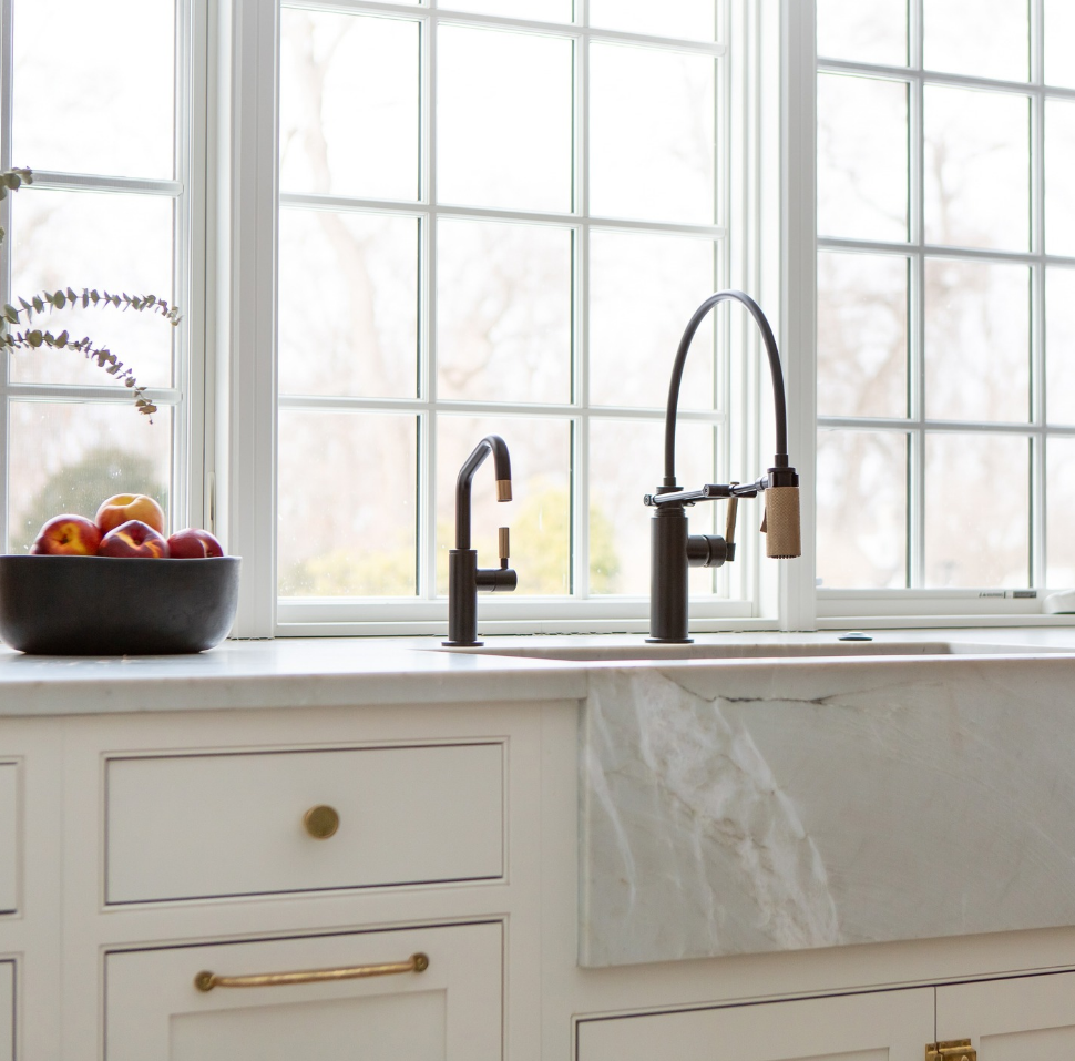 A kitchen sink with a bowl of fruit on the counter
