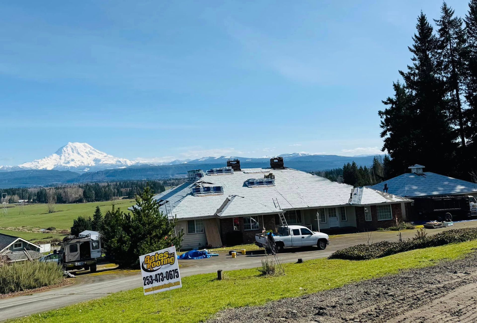 A white truck is parked in front of a house with a snowy mountain in the background.