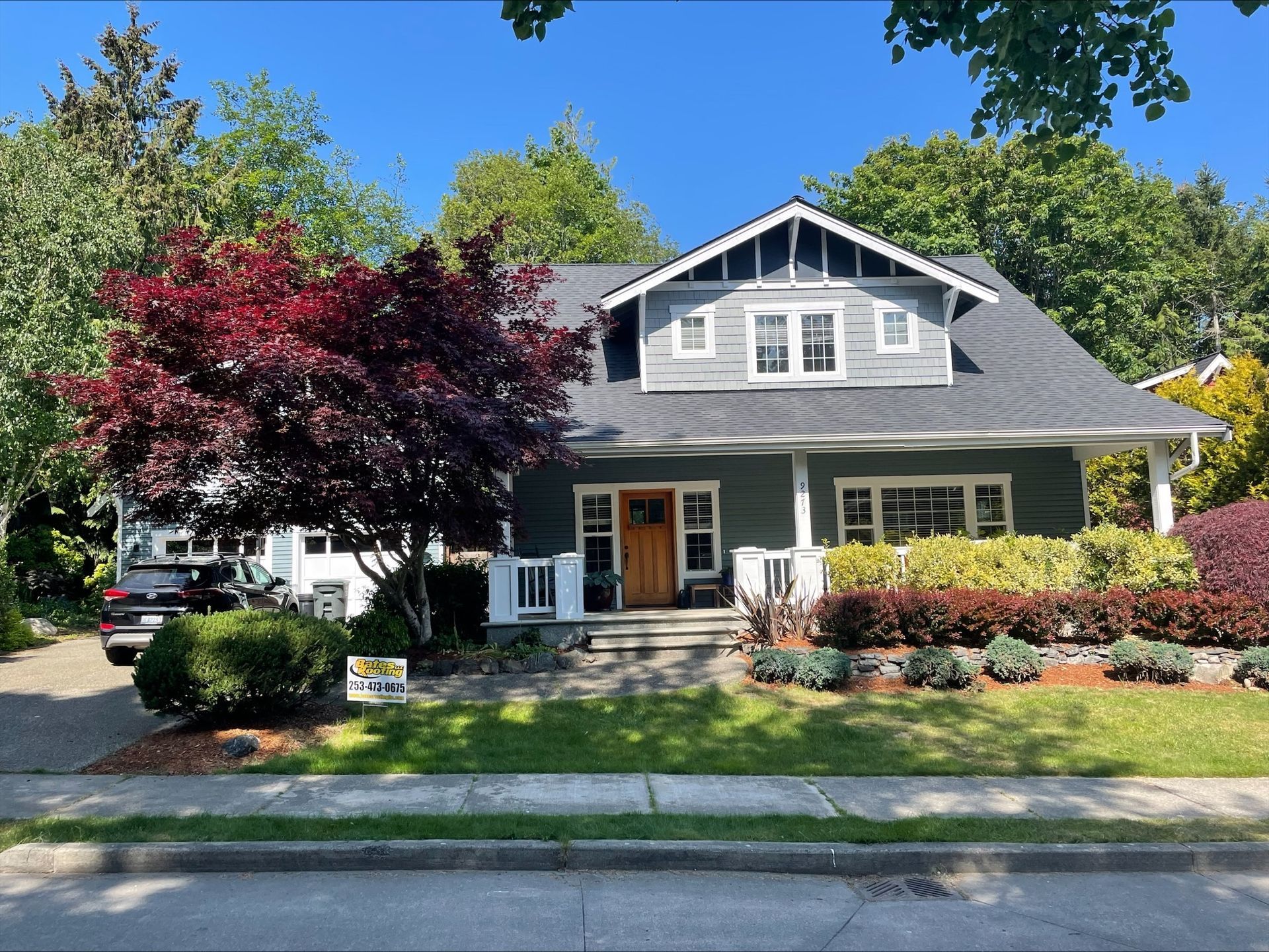 A large house with a gray roof is surrounded by trees and bushes.