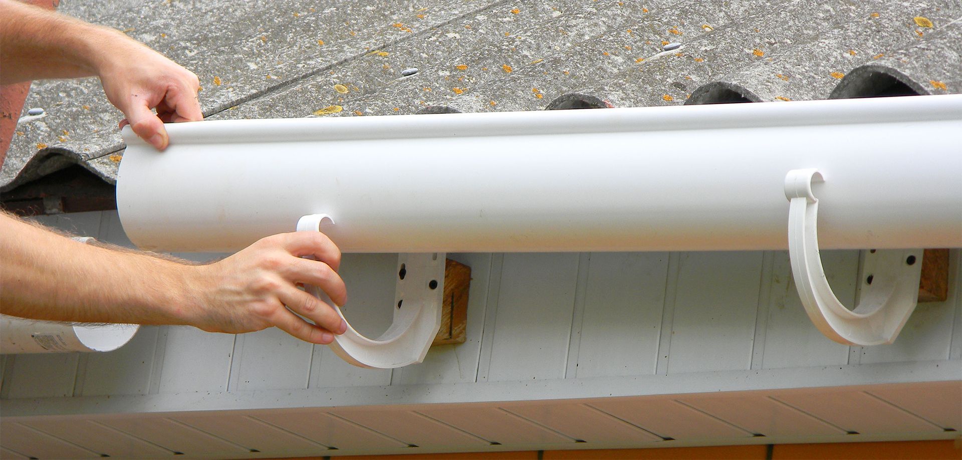 A man is installing a white gutter on a roof.
