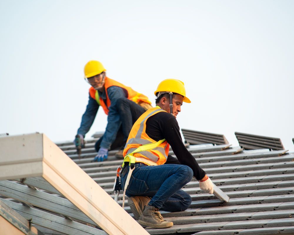 Two construction workers are working on the roof of a building.