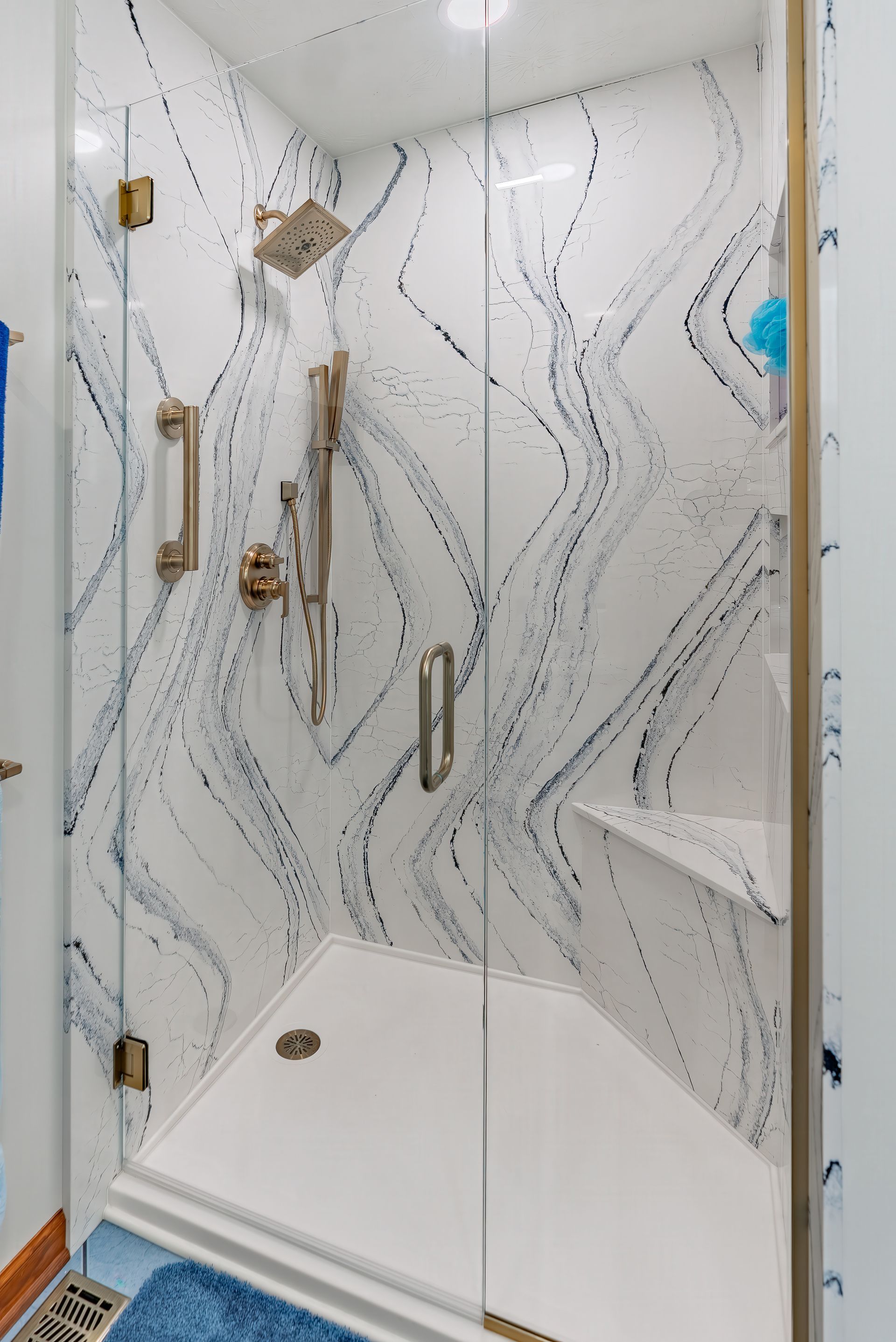 Shower with white and blue swirled tile, clear glass doors, and gold fixtures.