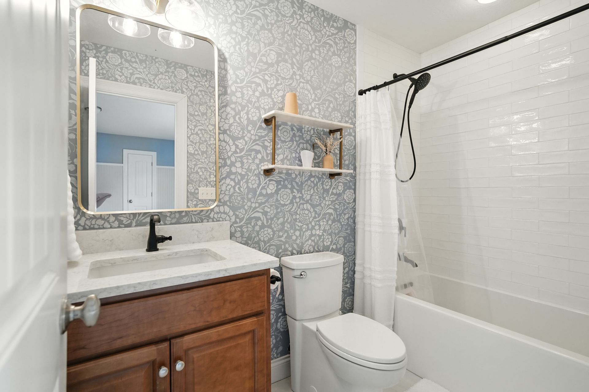 Bathroom with floral wallpaper, brown vanity, white toilet and tub with a shower curtain.