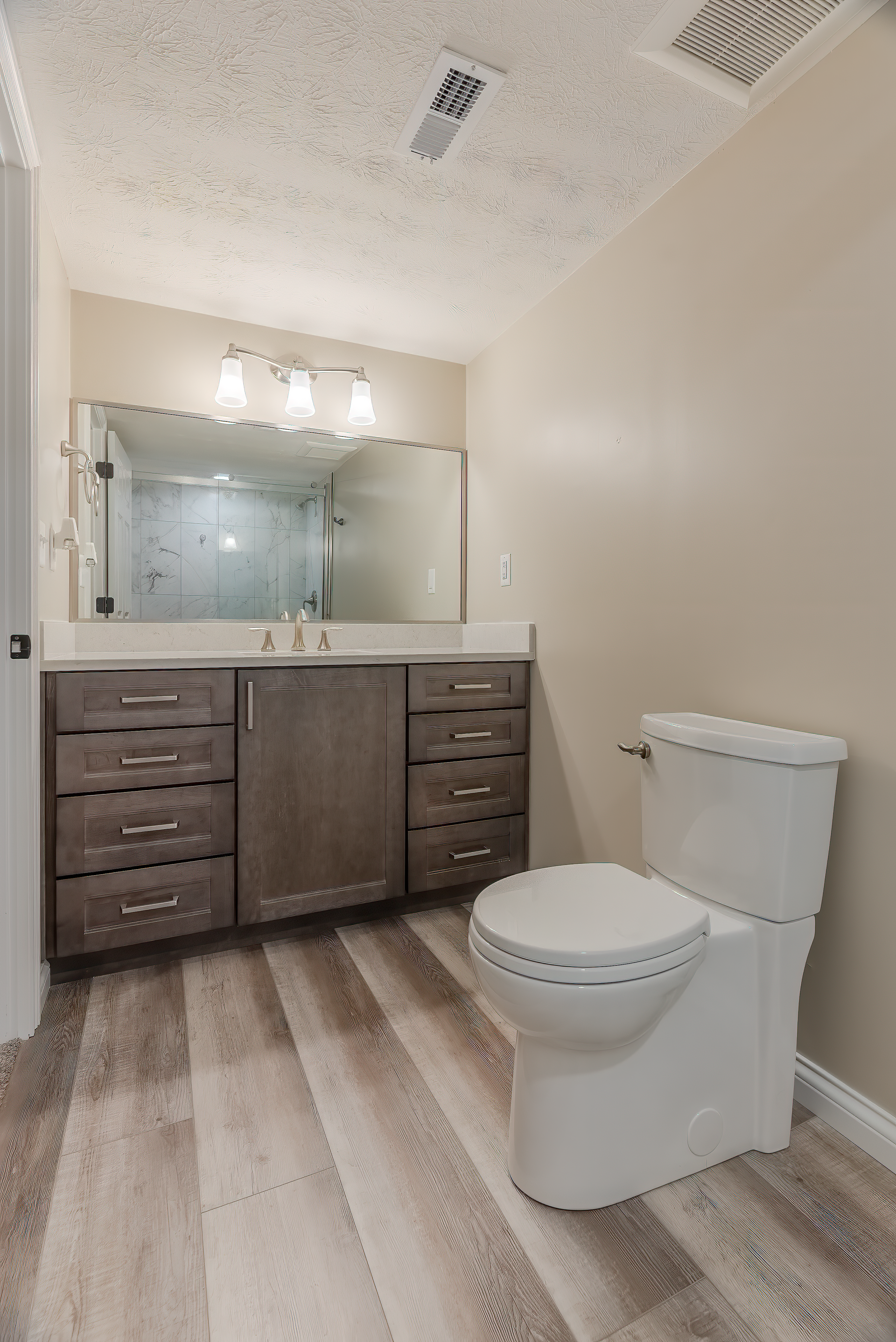 Bathroom with gray vanity, toilet, large mirror, and wood-look flooring. Beige walls and white ceiling.