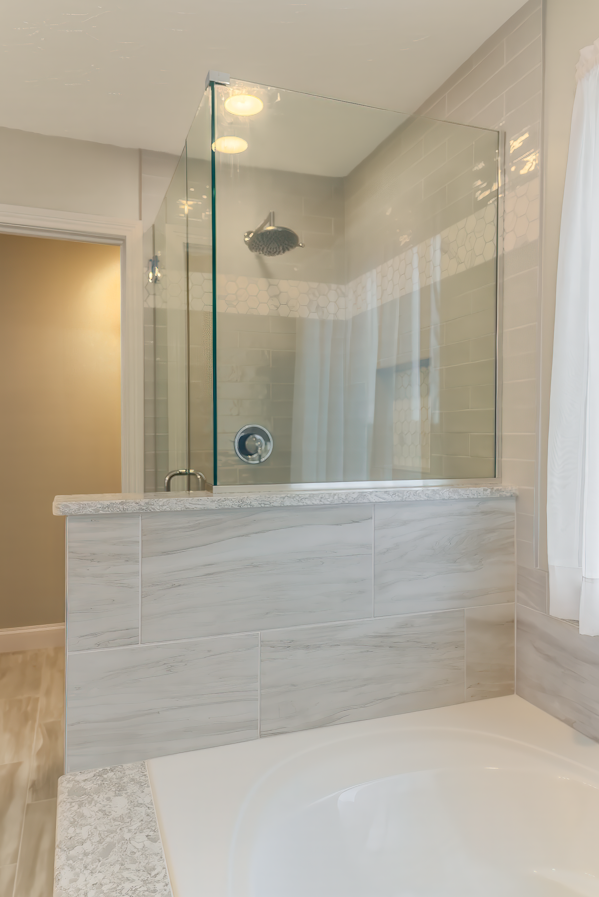Modern bathroom with glass shower, light gray tile, and bathtub.