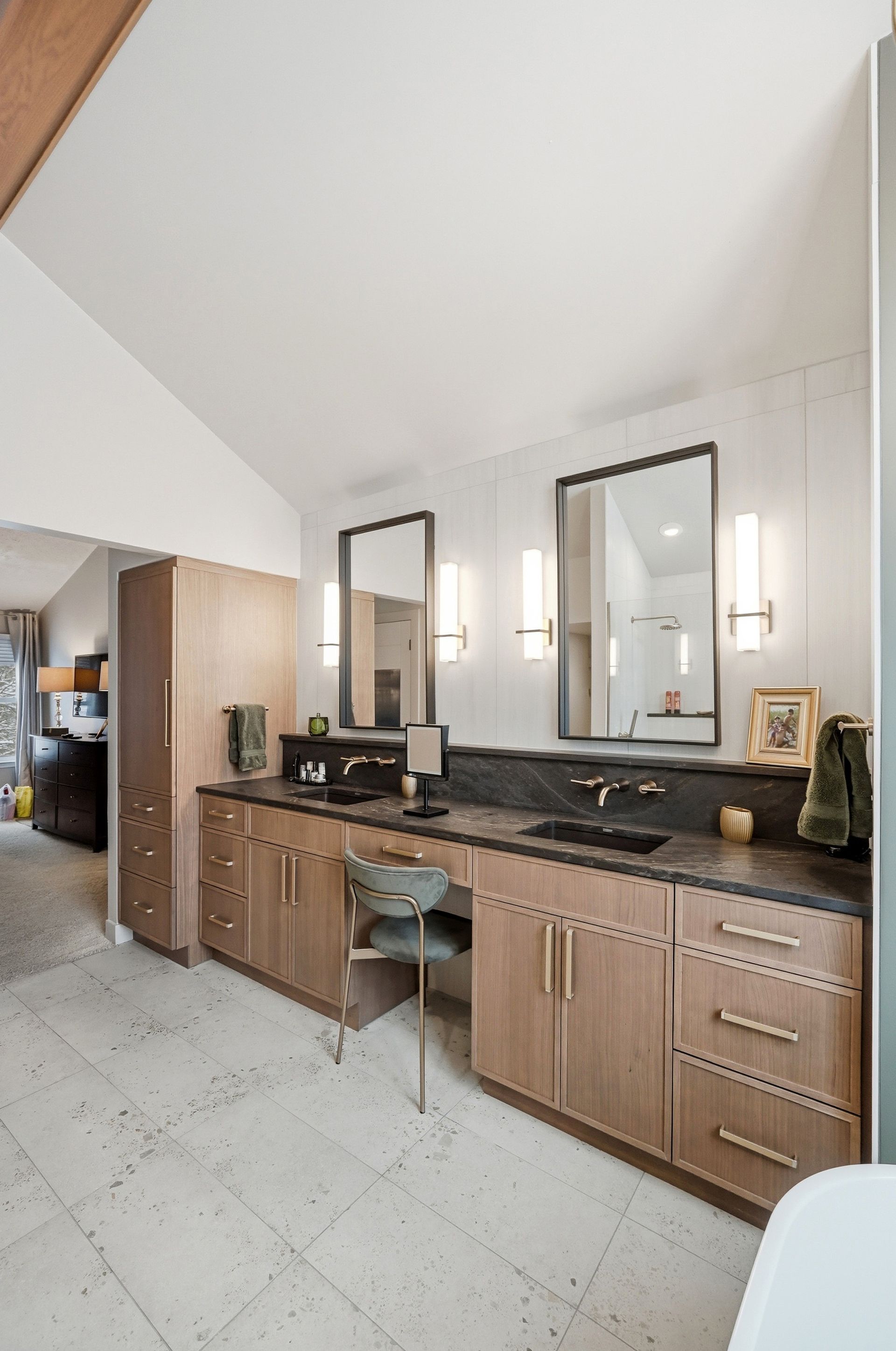 Bathroom with double vanity, black countertops, wood cabinets, and two mirrors.
