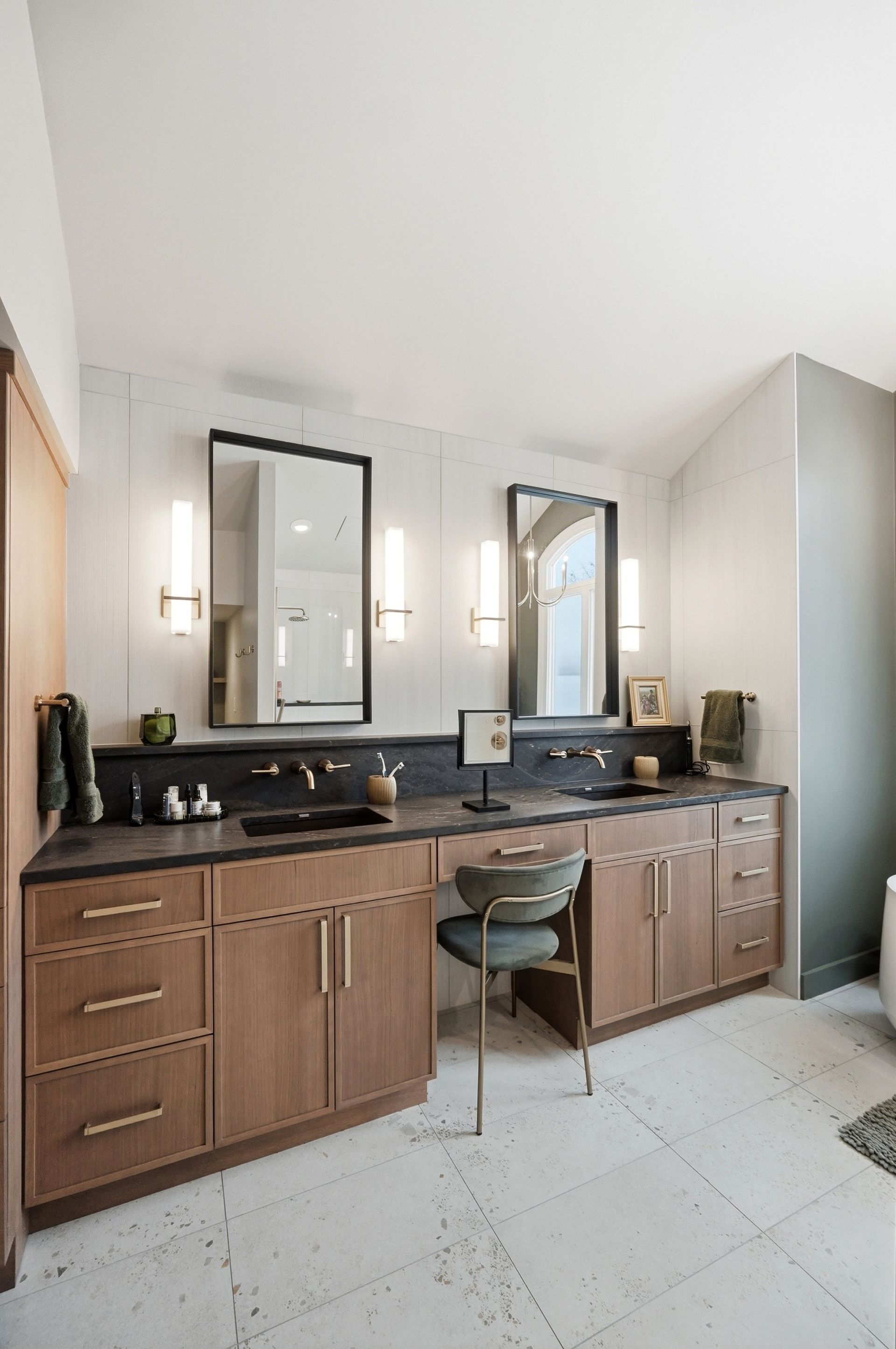 Bathroom with double vanity, two mirrors, and a makeup area. Wood cabinets, black countertop, and gold accents.