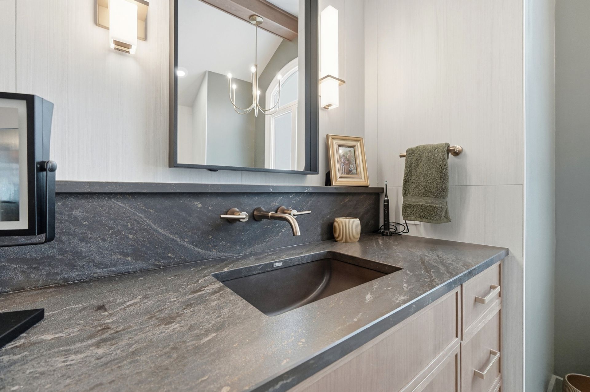Bathroom with dark gray countertop, rectangular mirror, and a wall-mounted faucet over a built-in sink.
