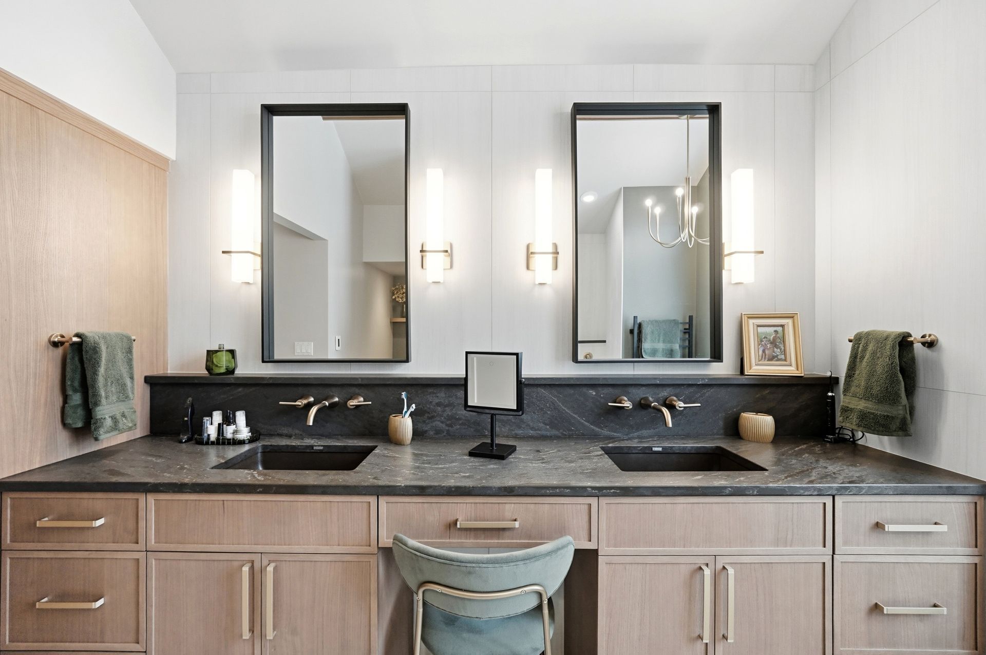 Bathroom with two sinks, mirrors, and sconces. Light wood cabinets with dark countertops.