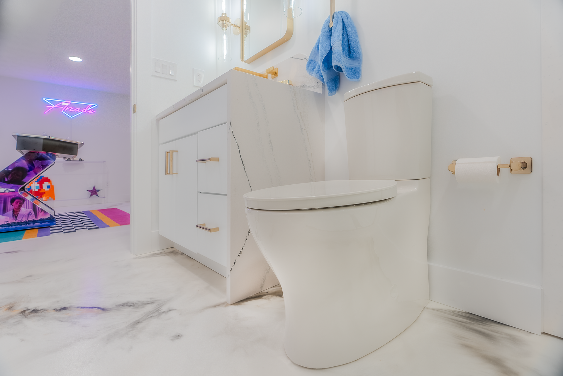 White toilet and vanity in a bright bathroom with gold fixtures. Playroom in the background.