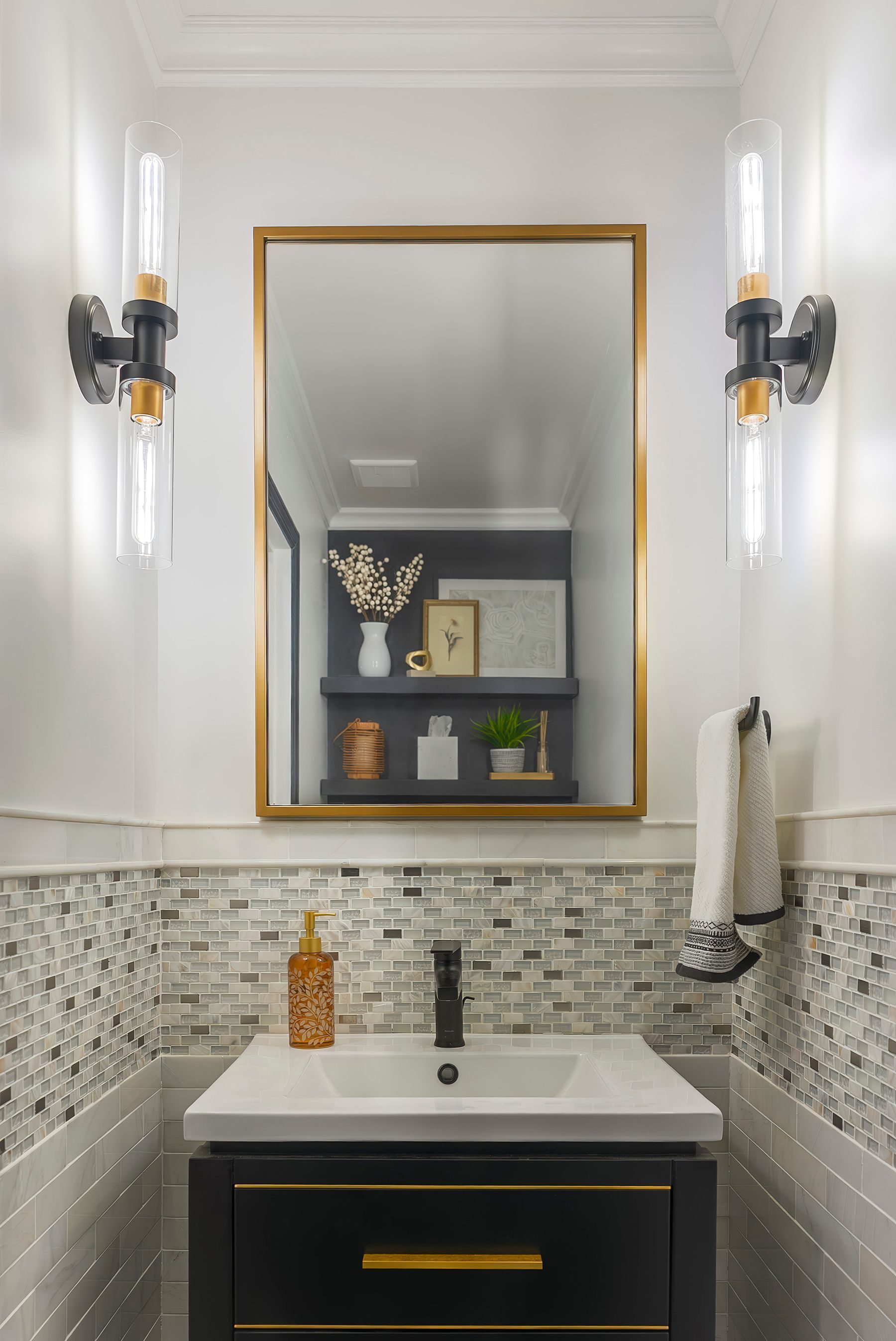 Bathroom with black vanity, gold-framed mirror, and industrial-style wall sconces.  Mosaic tile backsplash.
