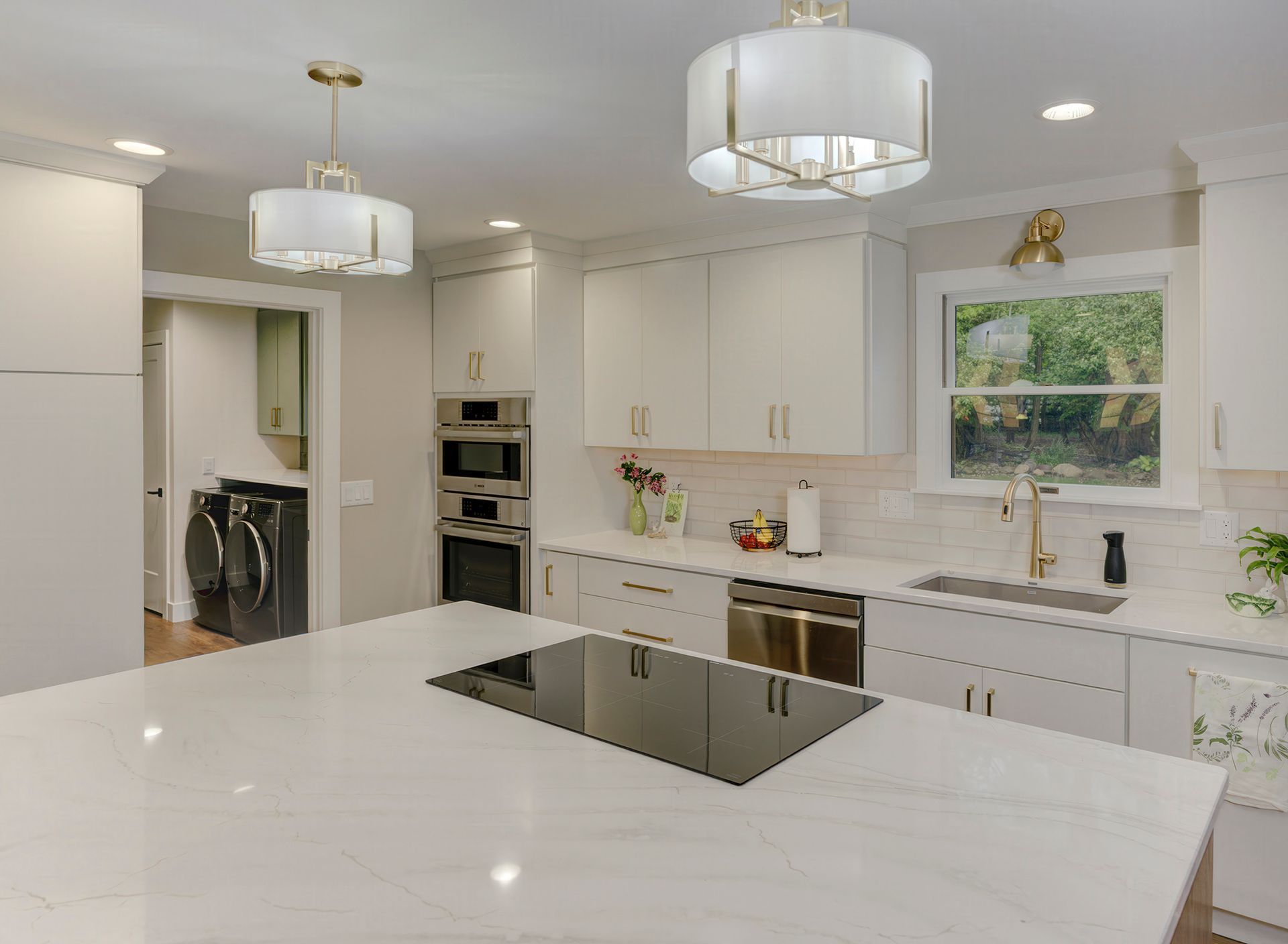 Modern white kitchen with island, cooktop, and gold accents.