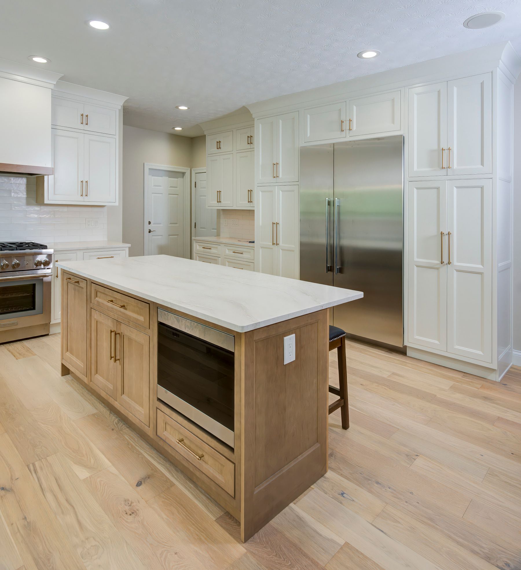 Kitchen with wood island and light cabinets, stainless steel refrigerator, light wood floor.