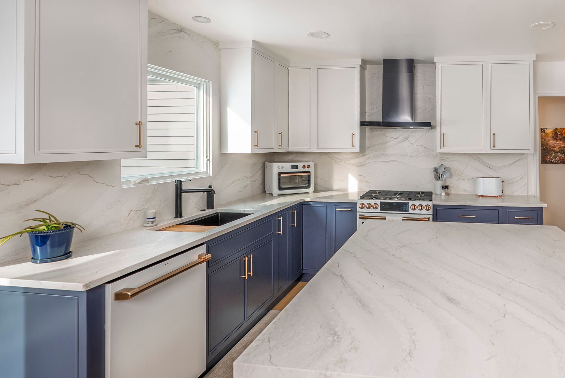 Modern kitchen with white and navy blue cabinets, marble countertops, and stainless steel appliances.