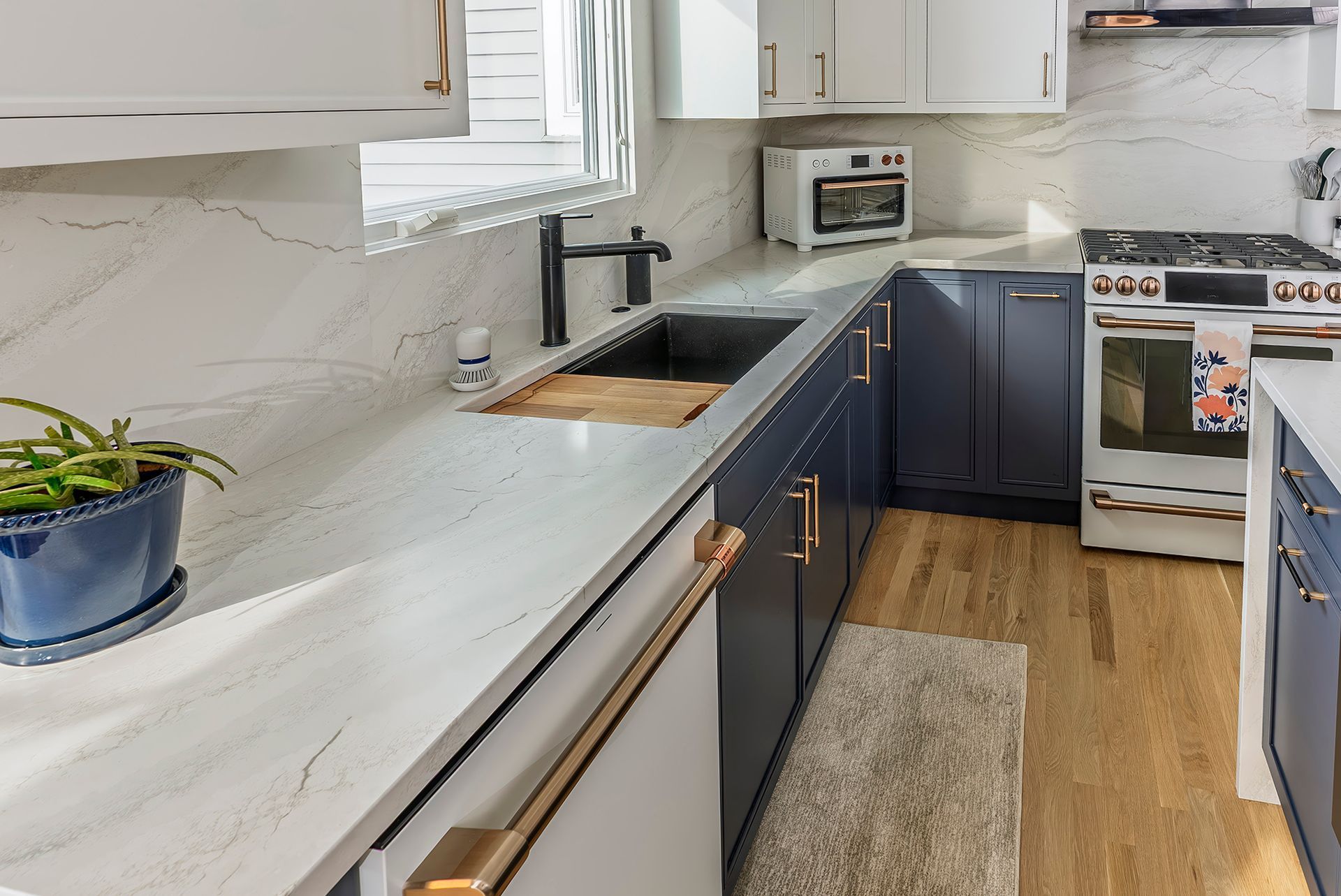 Kitchen with white countertop, navy cabinets, stainless steel appliances, and gold hardware.