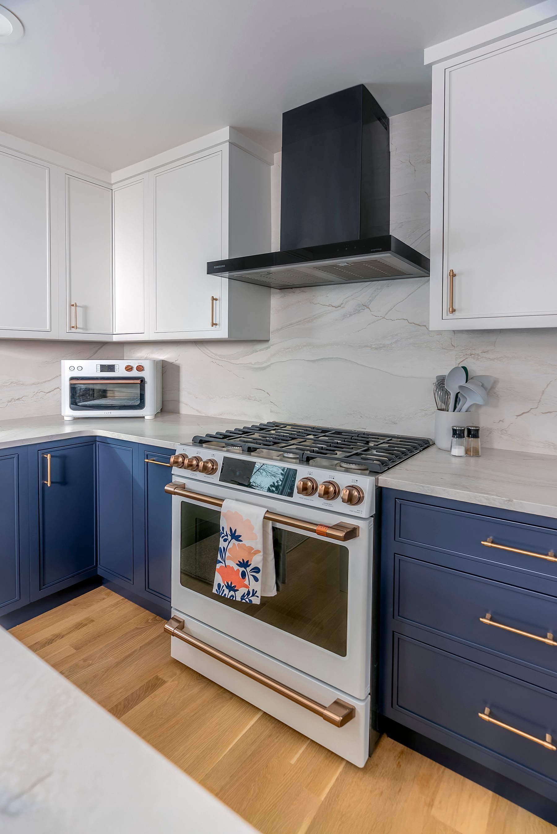 Blue and white kitchen with a white range, black vent hood, and gold hardware.