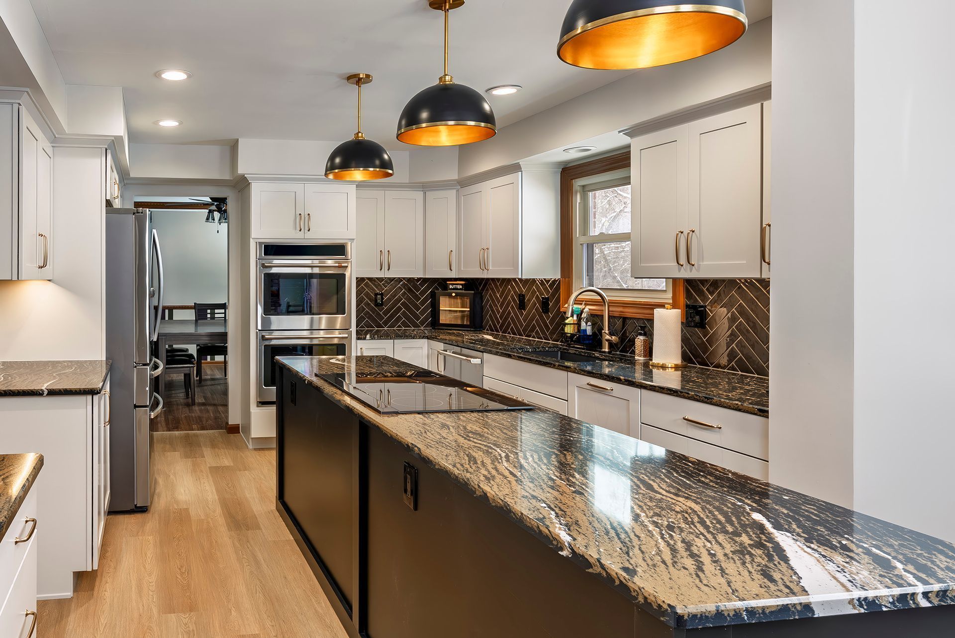 Modern kitchen with black island, granite countertops, white cabinets, and gold pendant lights.