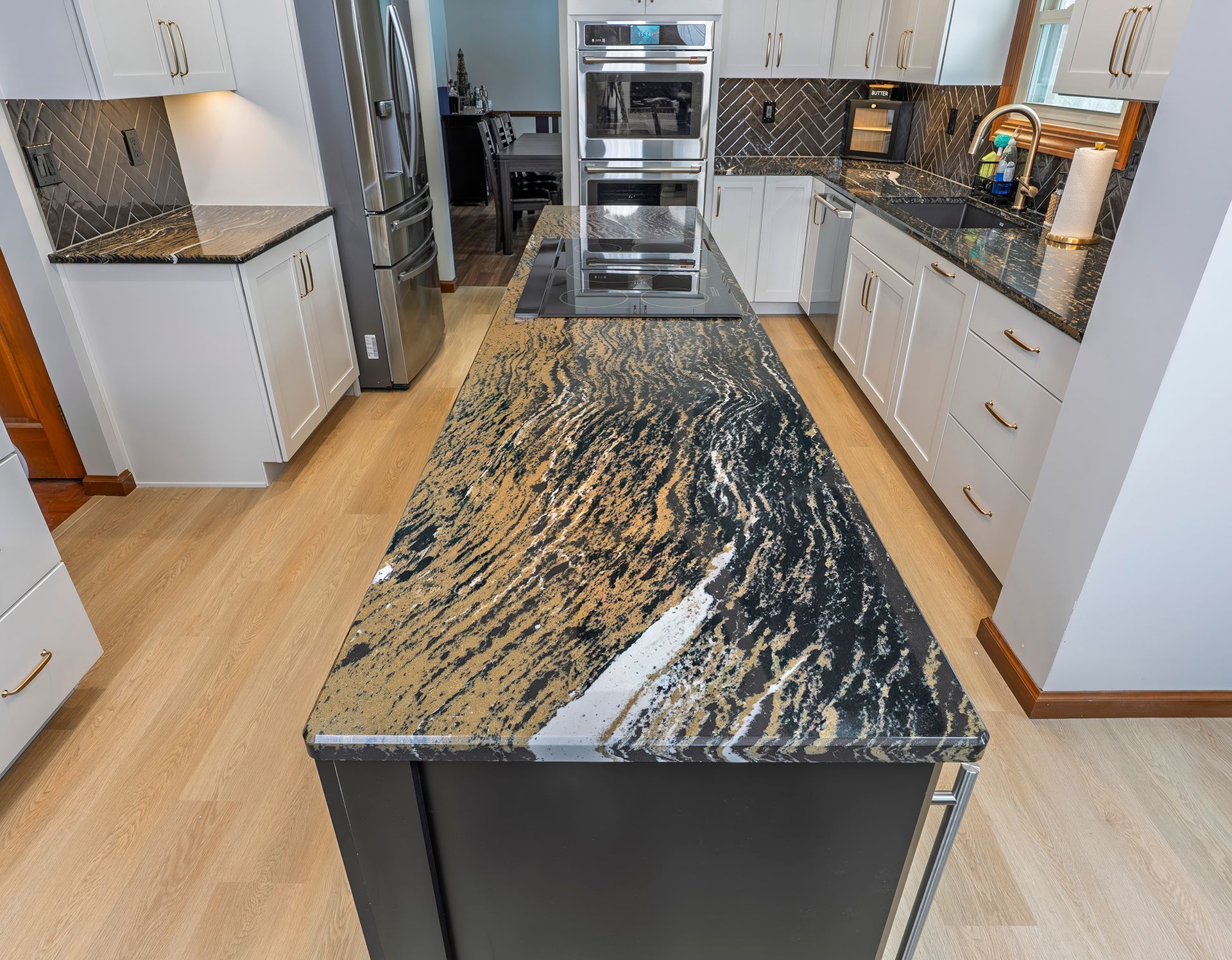 Kitchen with a black and gold granite island, white cabinets, stainless steel appliances, and wooden floors.