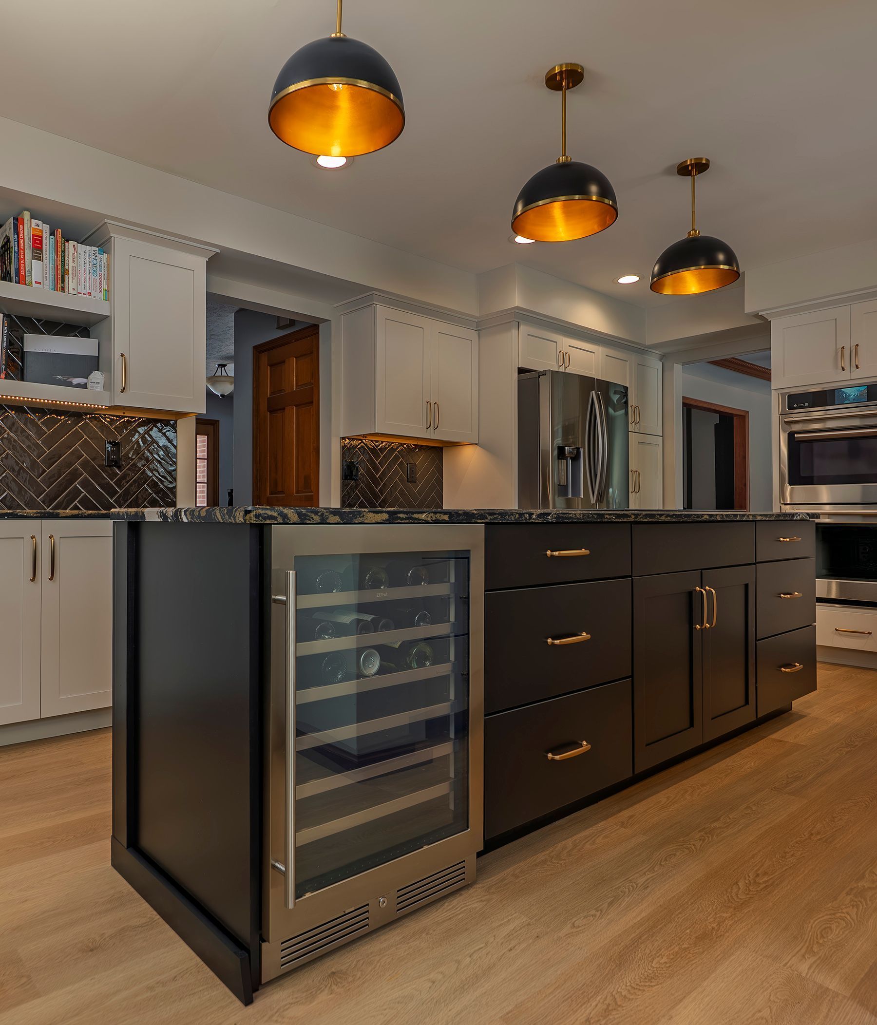 Kitchen island with wine fridge, black cabinets, and gold pendant lights.