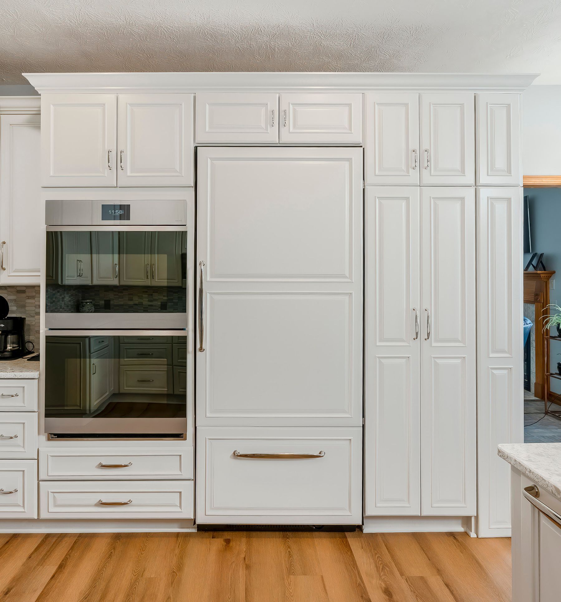 White kitchen cabinets surround a built-in refrigerator and oven on hardwood flooring.