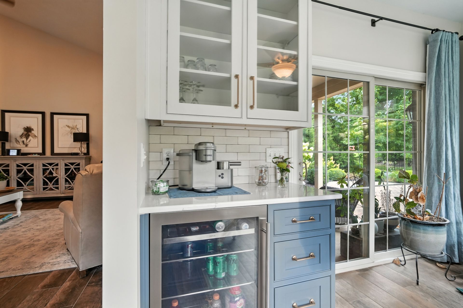 Kitchenette with blue cabinets, a mini-fridge, and white tile backsplash, next to a sliding glass door.