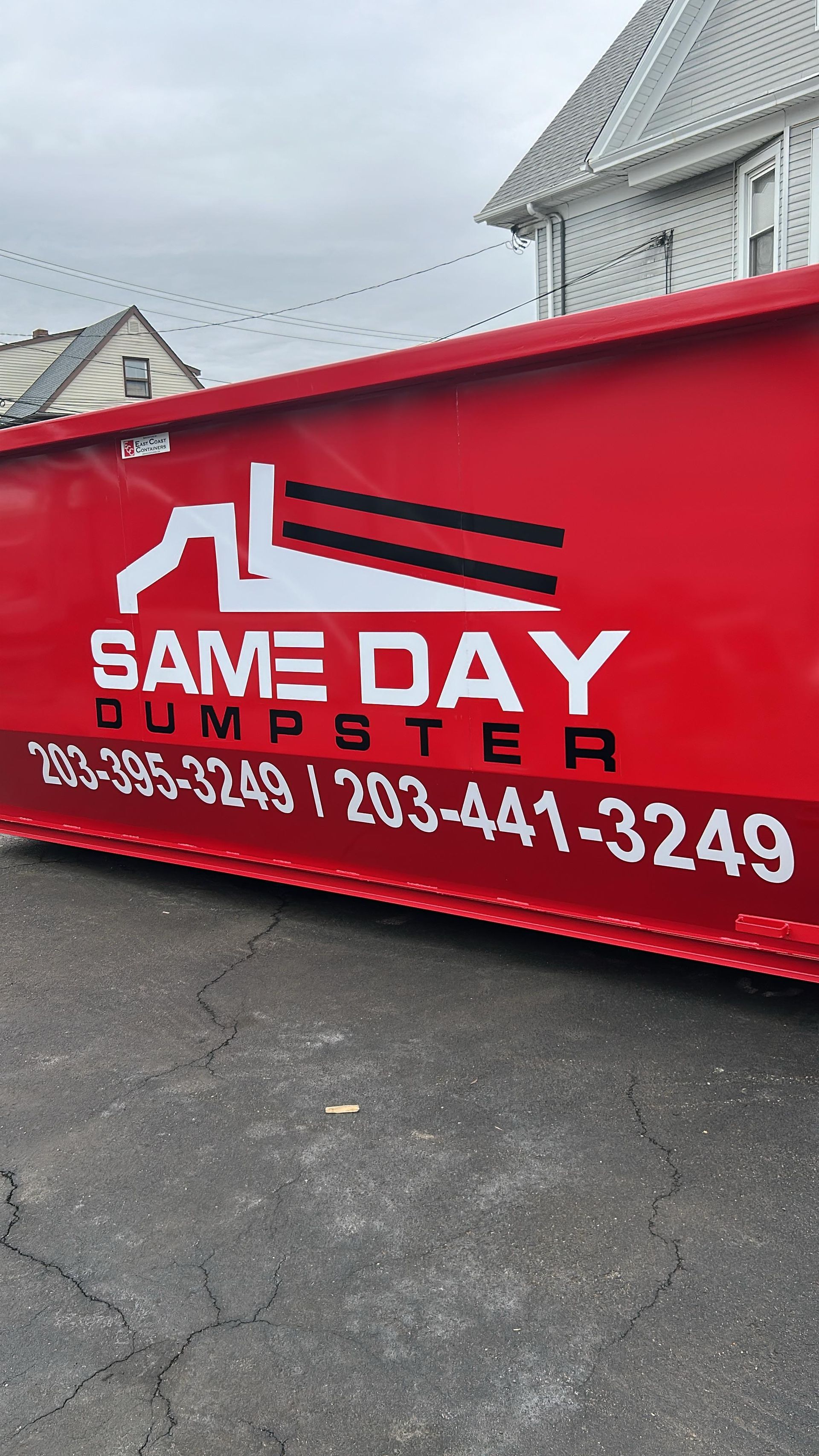 Red dumpster with "Same Day Dumpster" logo and phone numbers on asphalt.
