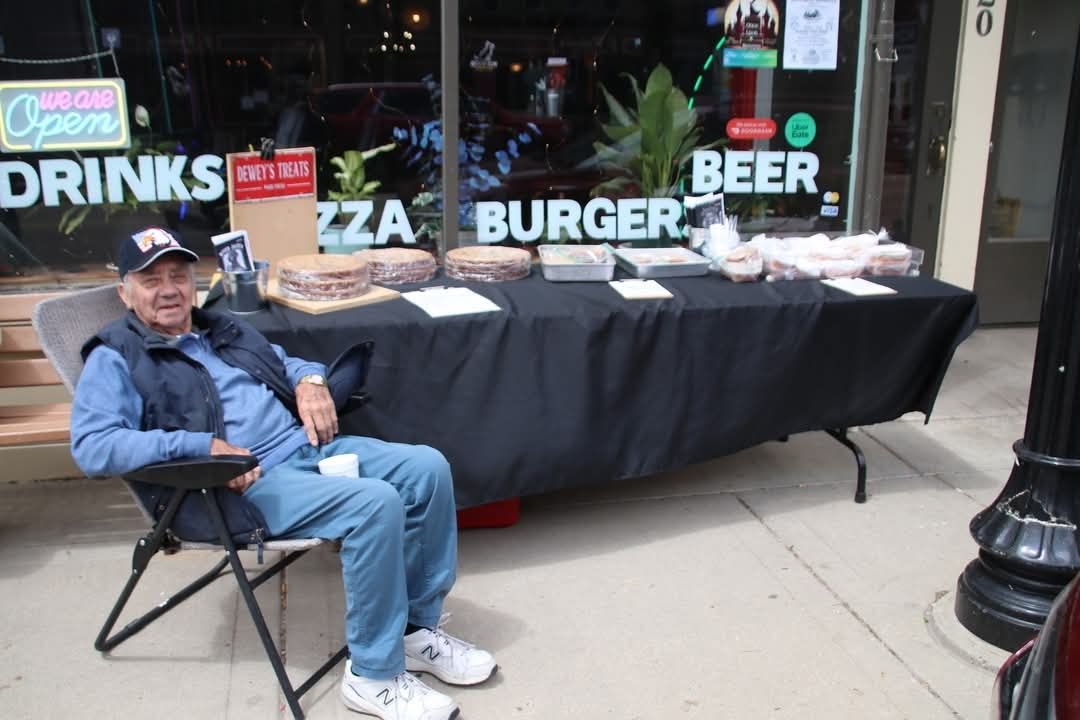 A man sits in a chair in front of a table that says drinks pizza burger beer