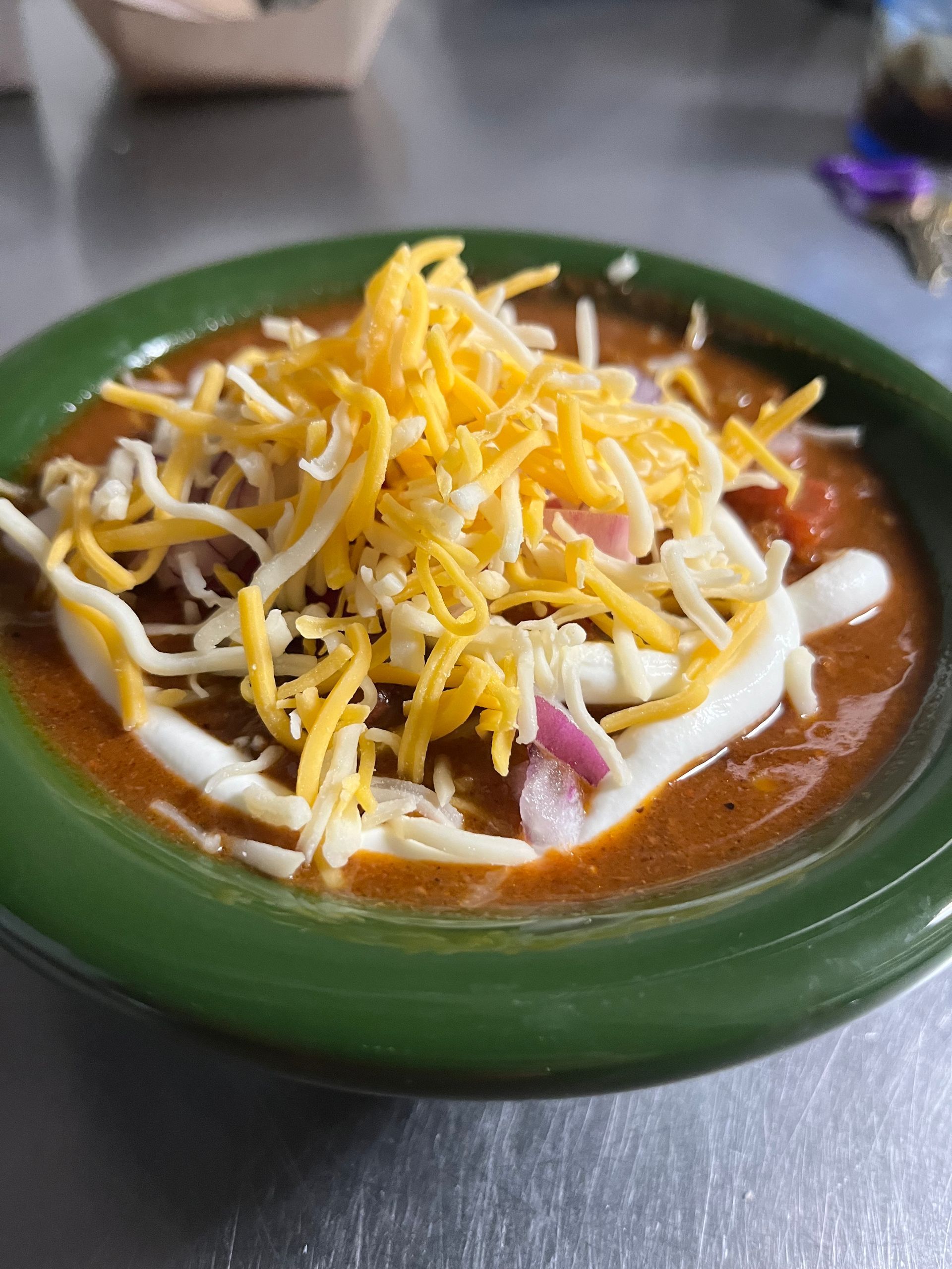 A bowl of chili with cheese and onions on a table.