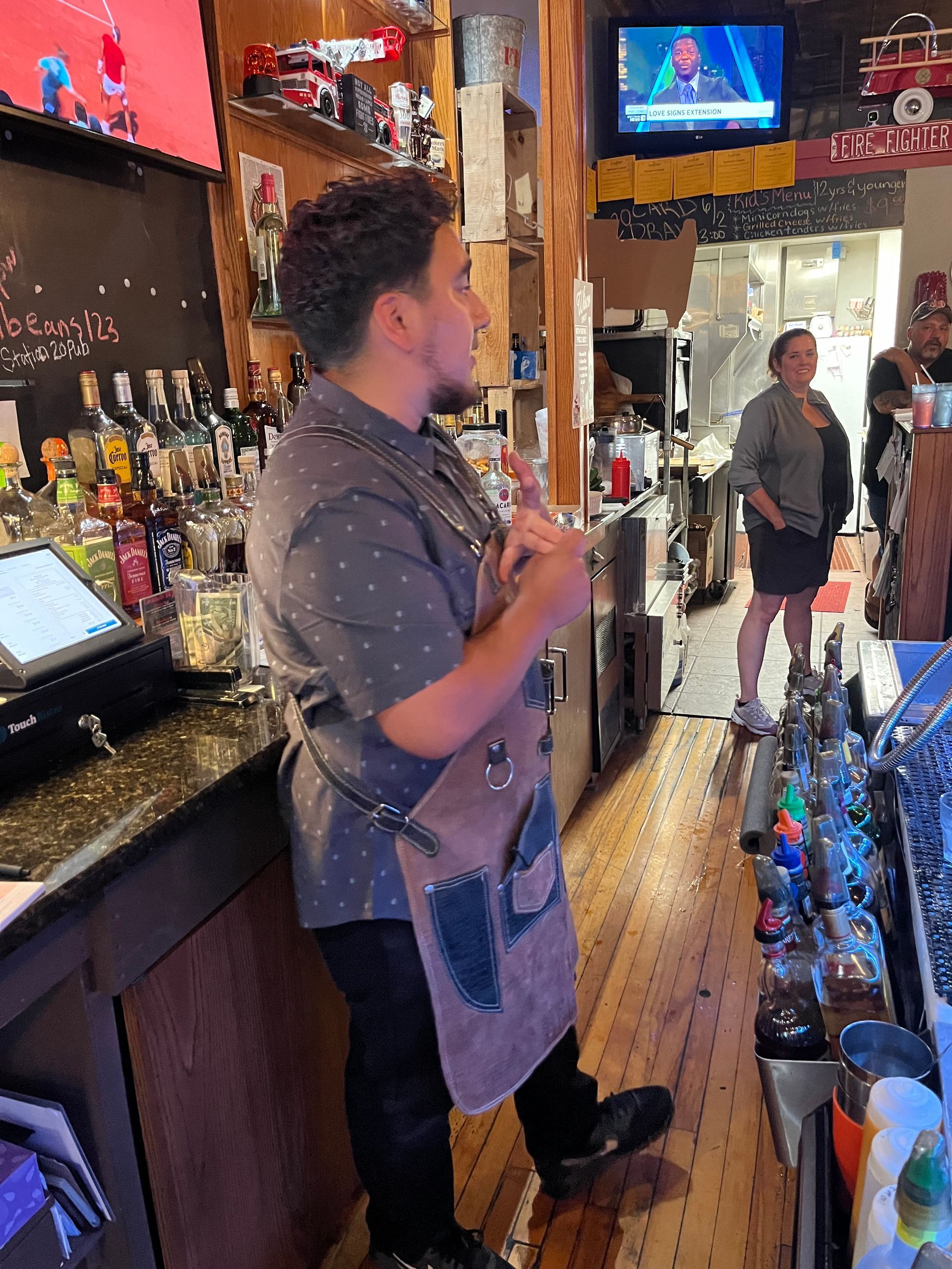 A man in an apron is standing in front of a bar.