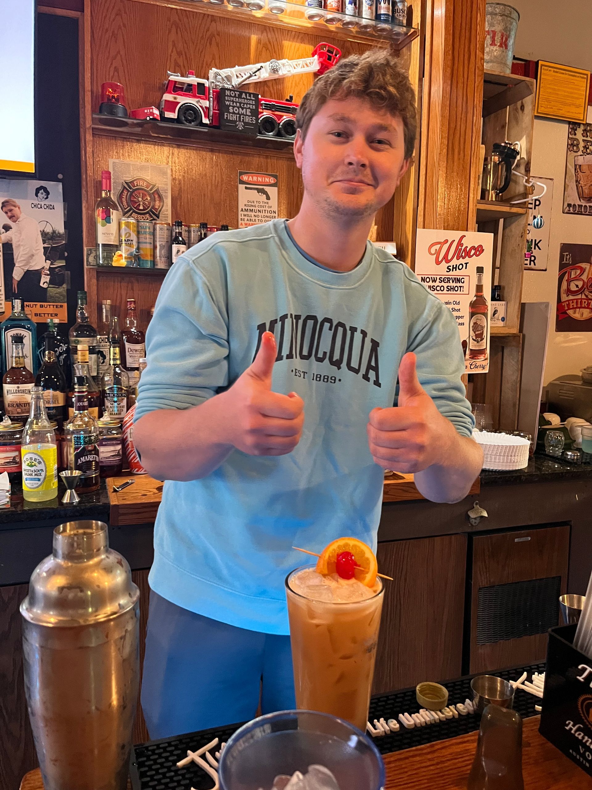 A man is giving two thumbs up while standing in front of a bar.