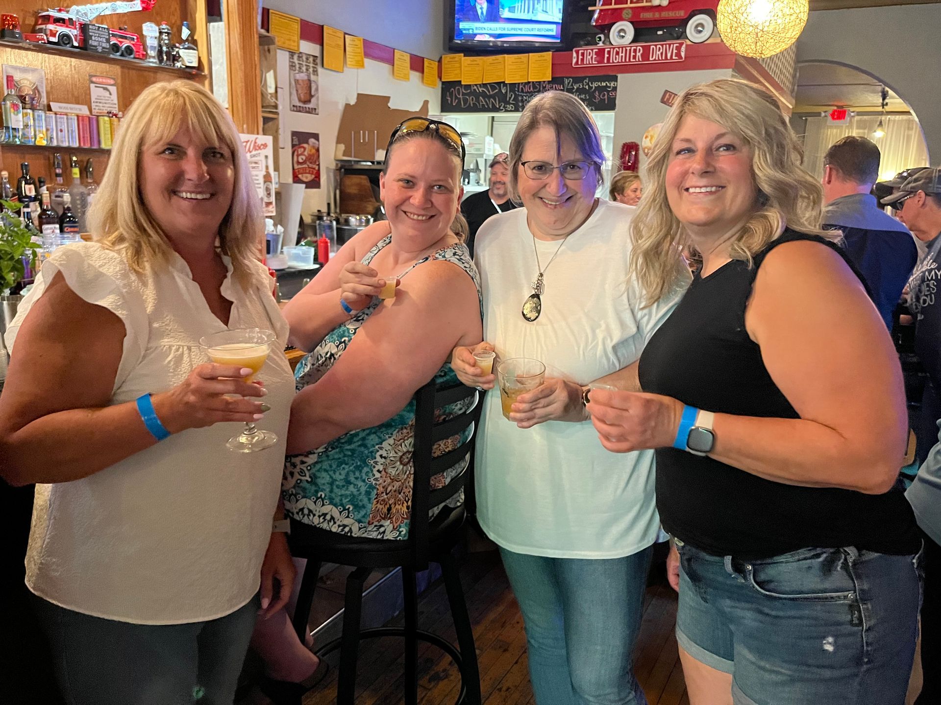 A group of women are standing next to each other in a bar holding drinks.