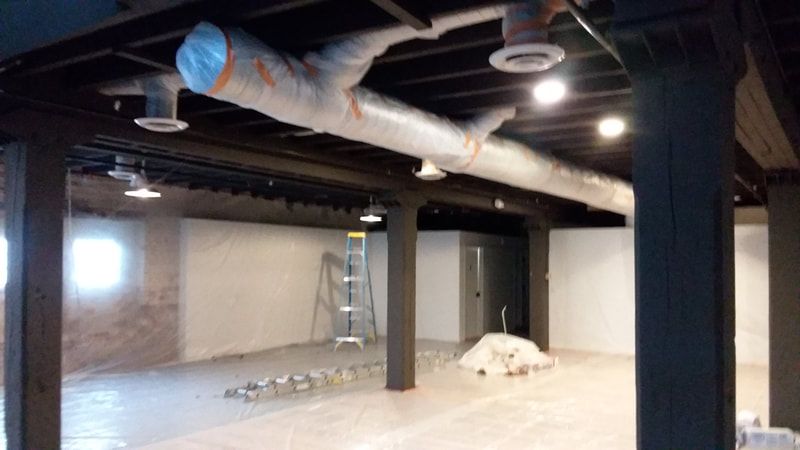 A large empty room with a ladder and a lot of pipes hanging from the ceiling.
