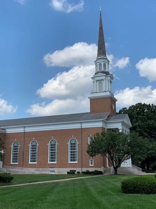A brick church with a steeple and a blue sky in the background