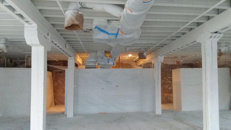 A large empty room with white columns and ducts hanging from the ceiling.