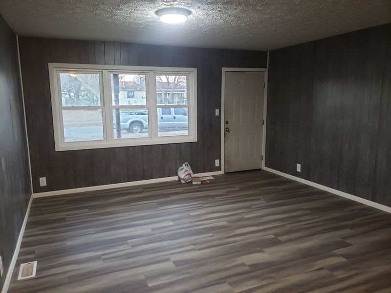 An empty living room with hardwood floors and a large window.