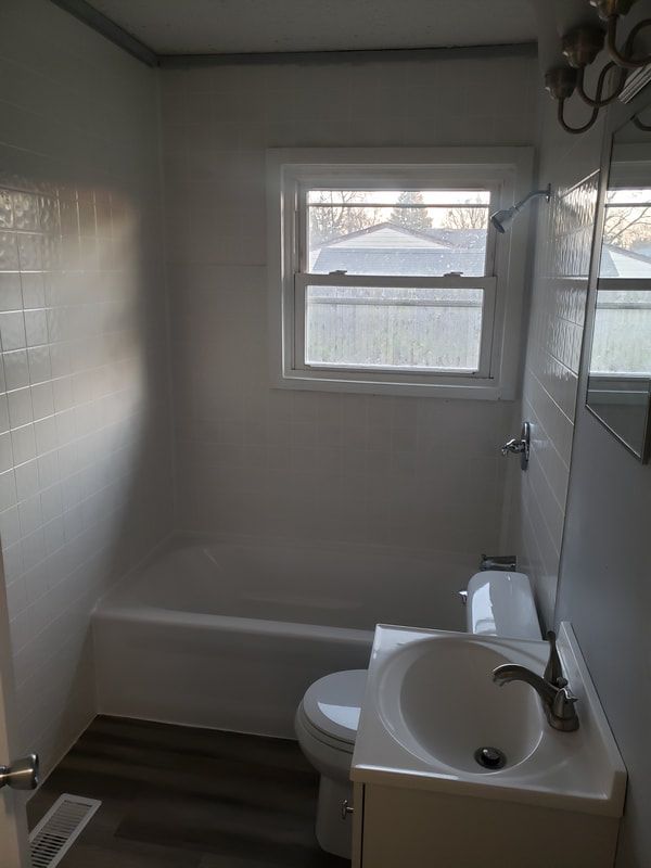 A bathroom with a toilet , sink , bathtub and window.