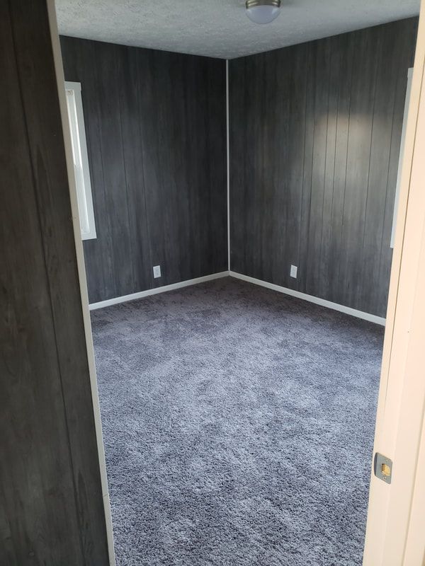 A bedroom with a gray carpet and wood paneling.